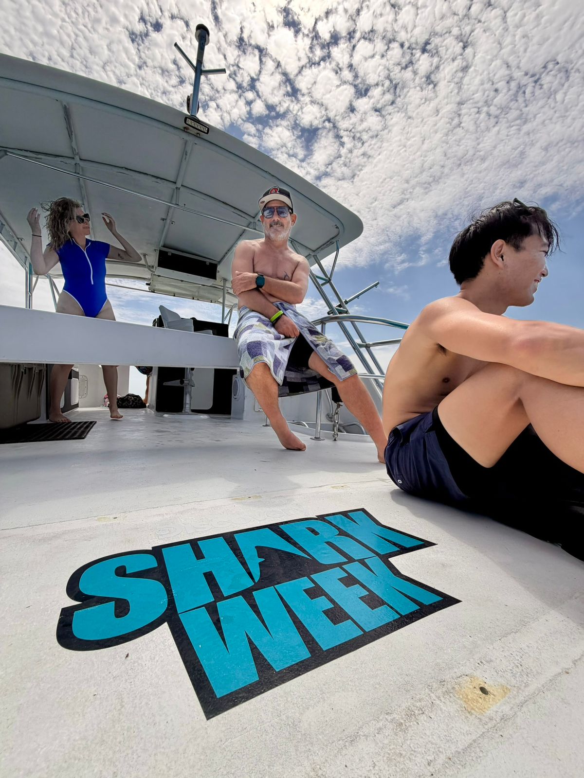 Divers relaxing on the deck of an expedition boat in Grand Bahama, with the Shark Week logo on the floor, ready for a tiger shark diving adventure. If you feel the call of the sea, this is your moment!.